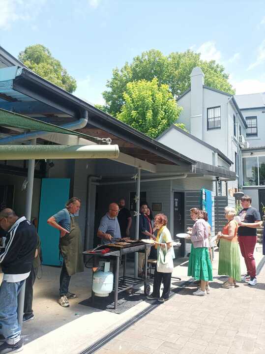 Volunteers in aprons cooking on a barbecue in the courtyard while a queue forms with plates