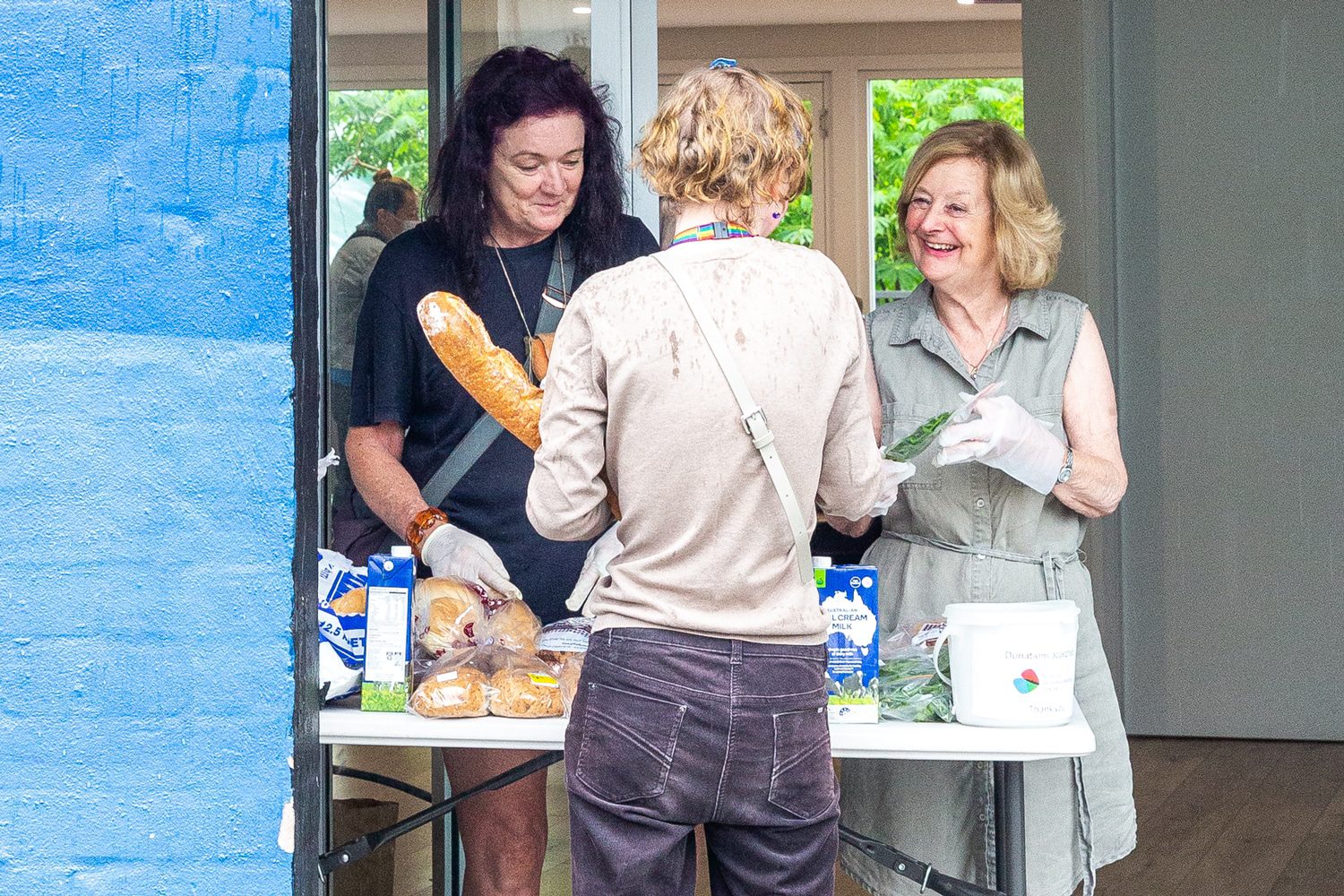 Volunteers handing out fresh bread and greens across a table at the community hub