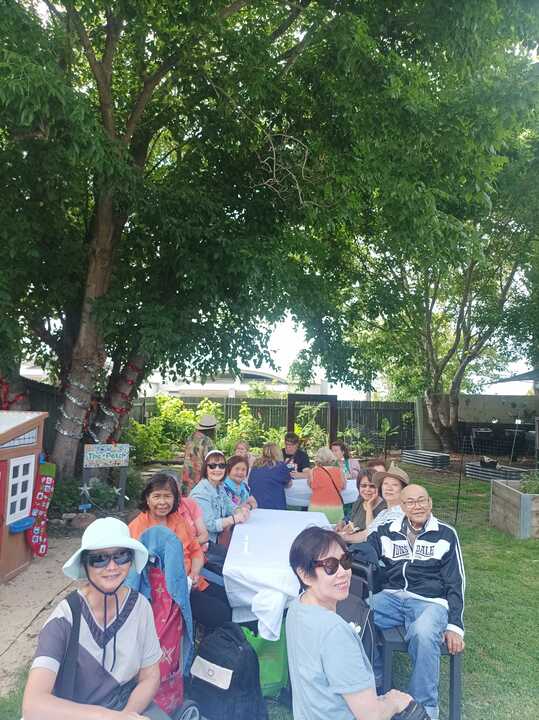 A long table under the trees in the Rozelle garden, ringed with people turning to smile at the camera