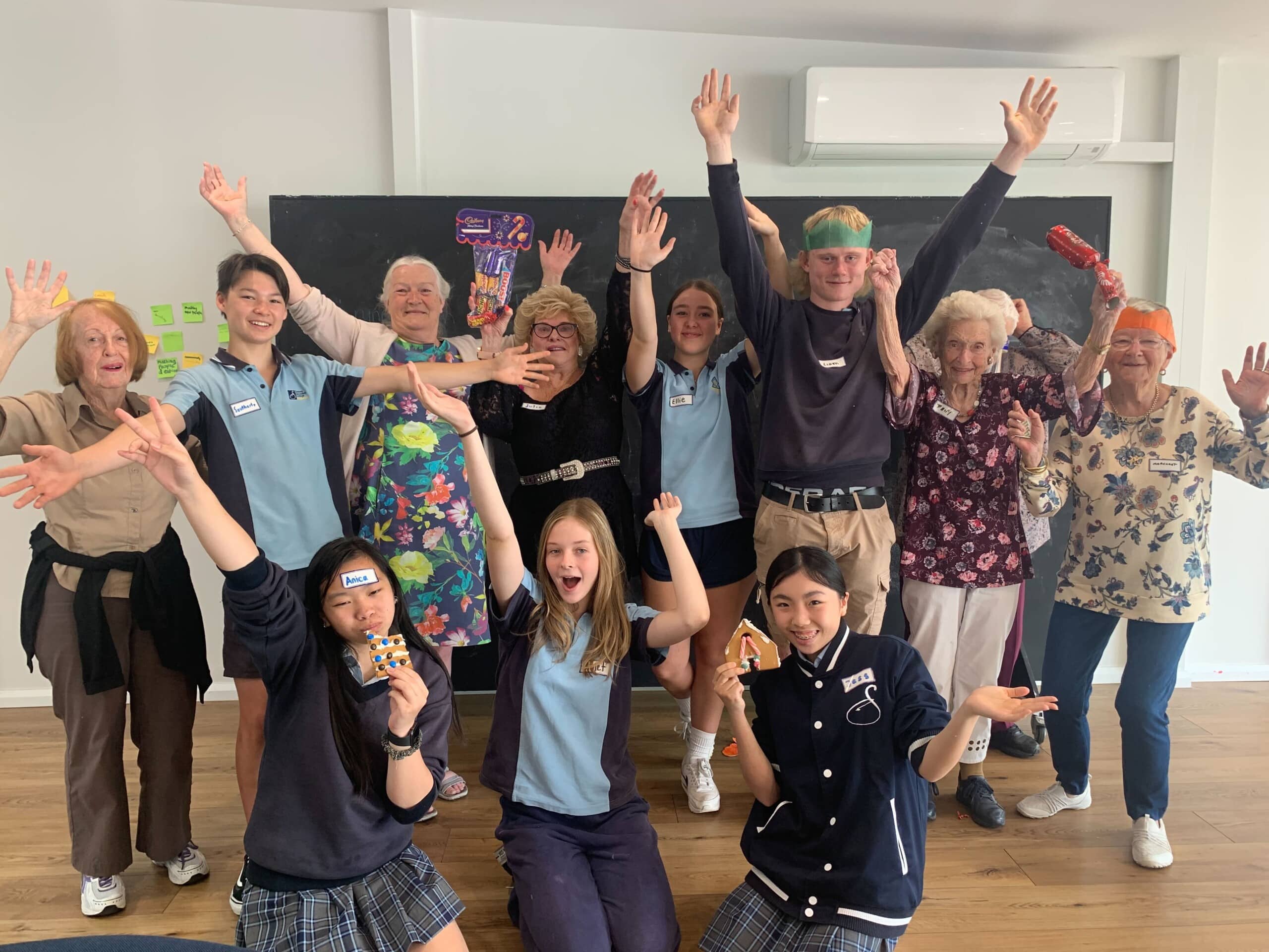 School students and older people together with their arms in the air, holding Christmas crackers and gingerbread they have decorated