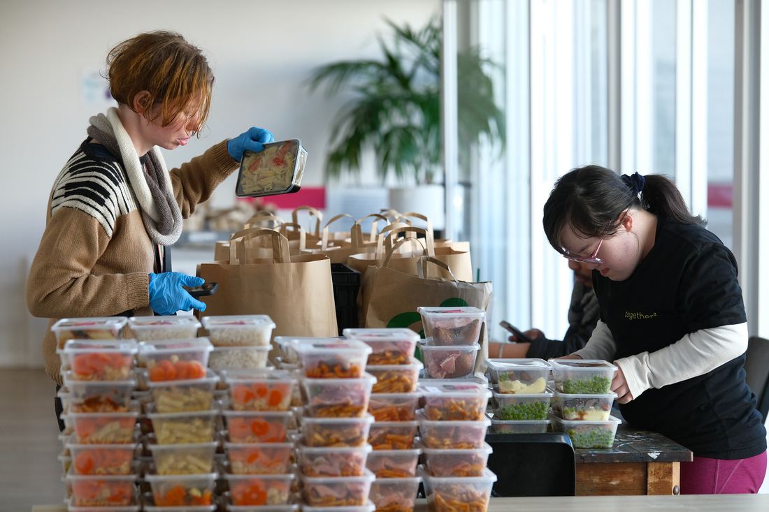 Two volunteers labelling and packing cooked meals into containers for delivery