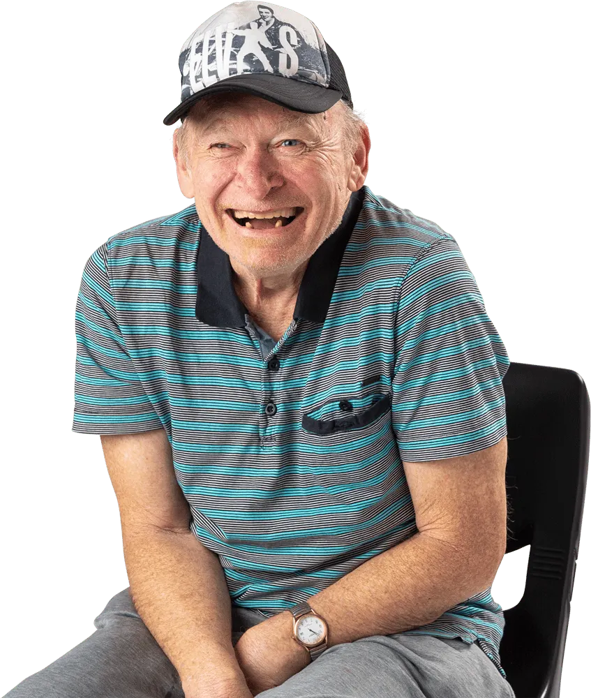 An older man in a baseball cap sitting and laughing, head tilted back