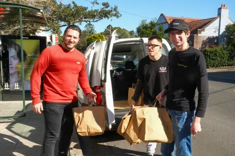 Three people carrying bags of meals beside a van
