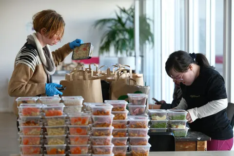 Two volunteers packing cooked meals into containers