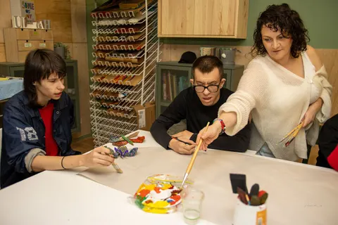 A support worker helping two people paint at a table
