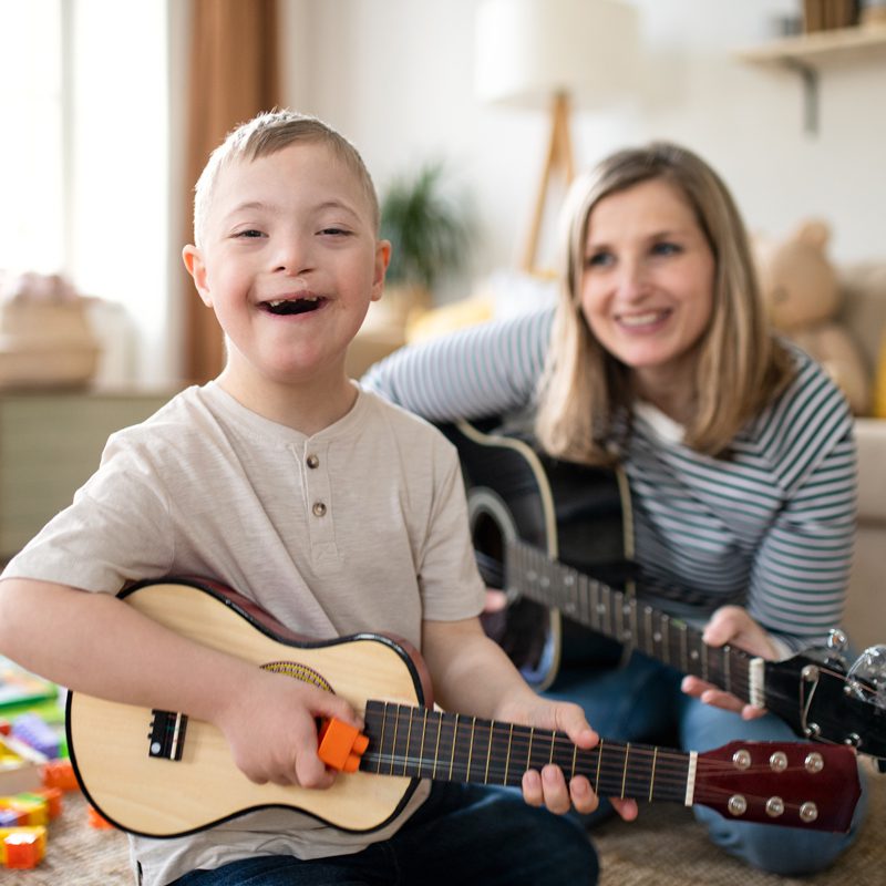 A smiling boy and a smiling woman playing stringed instruments together